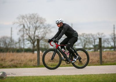 Vivid image of a cyclist riding a black and red bike outdoors in a rural setting with trees and fence in the background.