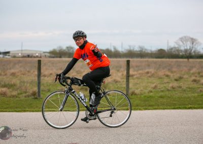 Bright orange bike race jersey and helmet, cyclist riding on a rural road during a cycling event.