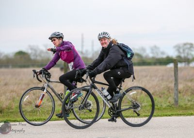 Women cycling on a bike trail during daytime, wearing helmets and outdoor gear for Bluebonnet Express event.