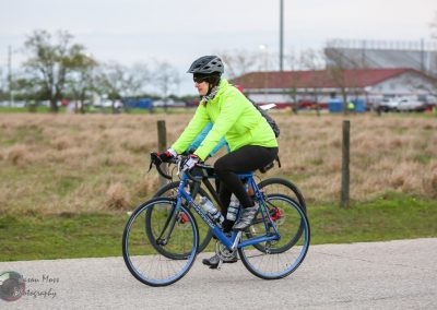 Bright yellow jacket cyclist riding Bluebonnet Express bike on paved trail during daytime.