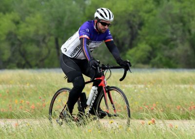 Cyclist riding a road bike in a scenic field with blooming wildflowers and lush green trees, promoting outdoor biking adventures.