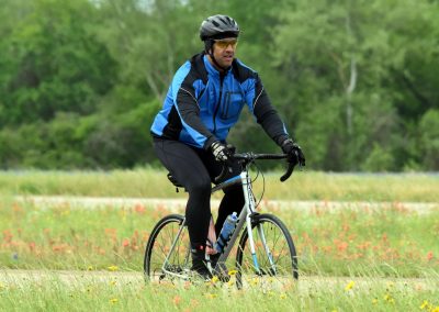 Vast outdoor scene of a man cycling through a lush green field filled with wildflowers, showcasing Bluebonnet Express biking experience.