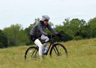Vibrant cyclist riding a mountain bike through wildflower field on Bluebonnet Express trail.