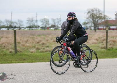 Bright woman riding a black and red bike outdoors, enjoying a cycling workout in cool weather.