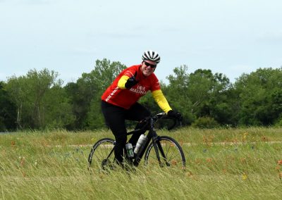 Vibrant cyclist riding through wildflower meadow with trees in background, promoting Bluebonnet Express bike tour.