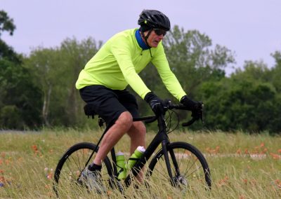 Vibrant cyclist riding in open field during daytime with greenery, promoting Bluebonnet Express bike trails.