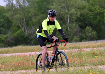 Vibrant cyclist riding on outdoor trail amidst colorful wildflowers and lush green trees.