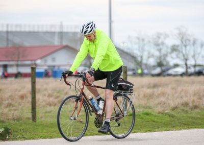 Bright yellow cycling jacket, cyclist riding bike on paved trail, outdoor fitness, active lifestyle image, Bluebonnet Express.