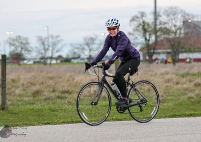 Comfortable woman riding Bluebonnet Express e-bike outdoors in a rural setting with trees and cloudy sky.