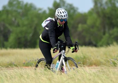 Vegan cyclist riding a mountain bike through a grassy field with trees in the background.
