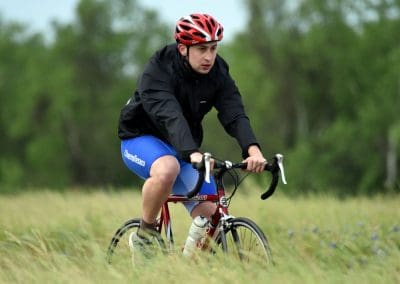 Young man cycling outdoors with a red helmet on a grassy trail, focused on the ride.