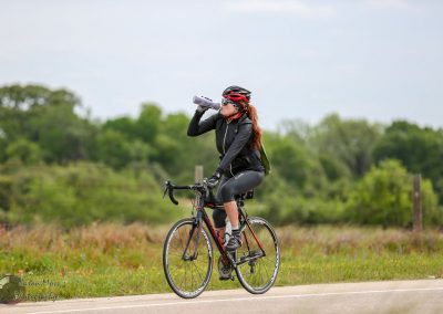 Vibrant woman cyclist drinking water on scenic trail during daytime.