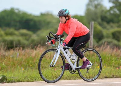 Bright woman riding a bike on outdoor trail, promoting Bluebonnet Express cycling service.