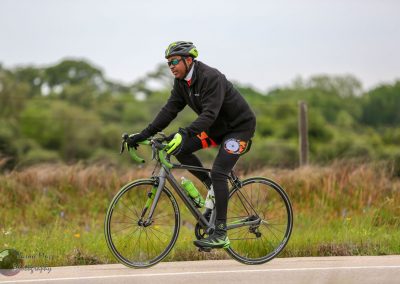 Vibrant cyclist riding a road bike on scenic outdoor trail with lush green landscape.