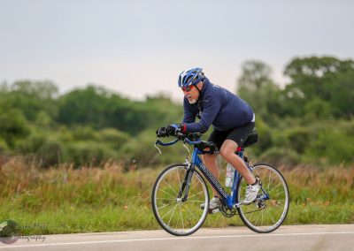 Vibrant cyclist riding on open road in green landscape, promoting Bluebonnet Express bike rides.
