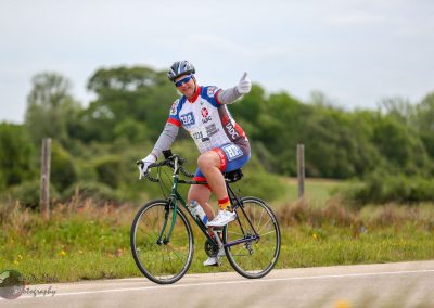 Bright cyclist on Bluebonnet Express bike ride, giving thumbs up in scenic rural setting, supporting cycling events.