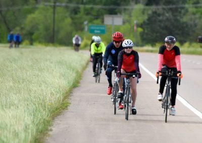 Vibrant cyclists riding on a scenic bike trail with greenery, promoting Bluebonnet Express cycling event.