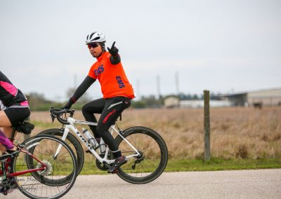 Brightly dressed cyclist riding a white bike in a rural setting with a cloudy sky.