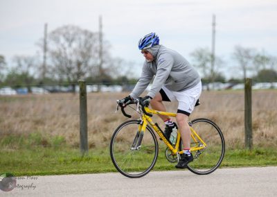 Bright yellow road bike on scenic outdoor trail during daytime with cyclist wearing gray hoodie and helmet.