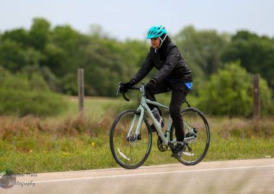 Female cyclist riding a bike outdoors on a scenic trail, promoting Bluebonnet Express bicycle tours.