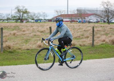 Rider on a blue bicycle wearing a helmet, face mask, and athletic gear during a cycling event.