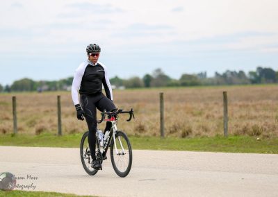 Rider on a road bike during a cycling event in a rural setting with open fields.