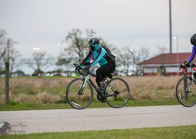Bright blue and black bike with cyclist wearing protective gear riding during daytime.