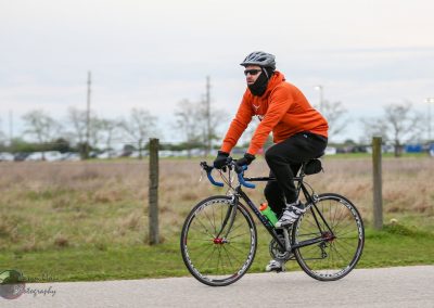 Bright orange hoodie cyclist riding on a paved trail in an outdoor park setting for Bluebonnet Express.