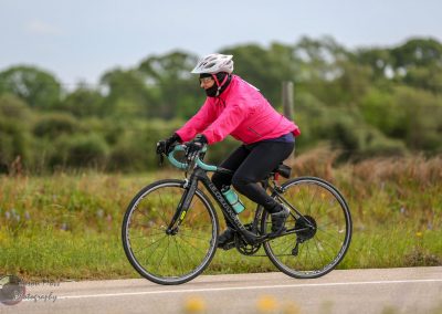 Bright pink jacket cyclist riding a mountain bike outdoors on a scenic trail.