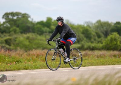 Efficient cyclist riding a road bike on a scenic rural trail during daytime.