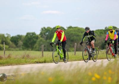 Brightly dressed cyclists riding on scenic rural road during daytime.