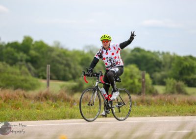 Bright cyclist in Polka Dot bike jersey riding through scenic countryside, promoting Bluebonnet Express bike tours.