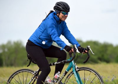 Vibrant female cyclist riding a blue bike during outdoor sport, wearing helmet and sunglasses.