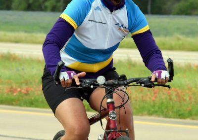 Bright woman riding a bike in blue and yellow jersey on scenic outdoor trail.