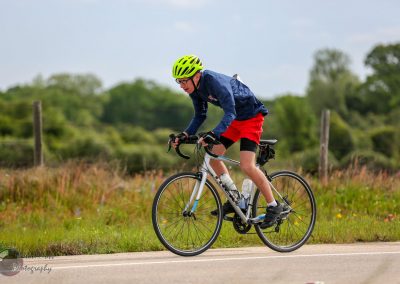 Bright yellow helmet, athletic cyclist, riding a bike outdoors along scenic rural road for Bluebonnet Express promotion.