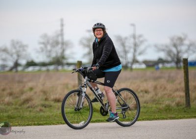 Smiling woman riding a bike on a scenic trail in outdoor setting, showcasing Bluebonnet Express cycling experience.