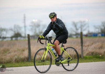 Bright yellow road bike with cyclist in black gear riding outdoors during daytime.