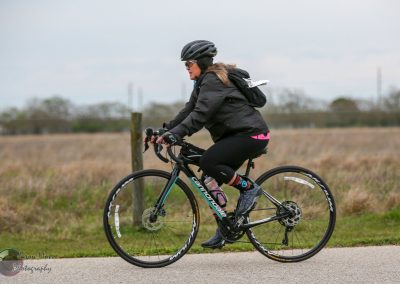 Bright bluebonnet express bike on scenic outdoor trail during cloudy weather, features a woman cycling.
