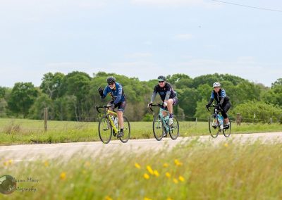 Vibrant cyclists riding on a scenic trail during daytime with lush green trees in the background.