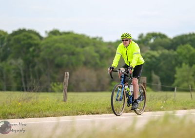 Bright yellow cycling jacket with reflective stripes worn by male cyclist riding on countryside road, emphasizing safety and outdoor adventure.