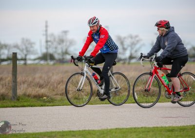 Cyclists riding along a paved trail in a scenic outdoor setting, promoting Bluebonnet Express cycling events and community fitness.
