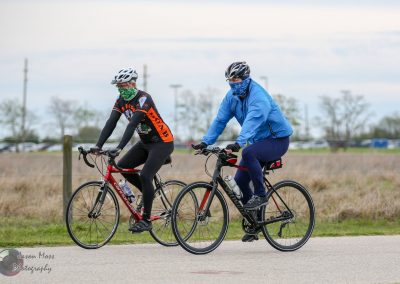 Helmets and face masks worn by two cyclists riding on a trail.