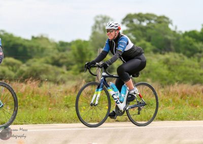 Bright woman riding Bluebonnet Express gravel bike on scenic rural trail, enjoying cycling adventure.