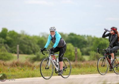 Bright female cyclists riding bikes outdoors on scenic trail, promoting Bluebonnet Express cycling event.