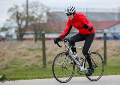 Velo cyclist riding on a paved trail, dressed in red jacket and black cycling gear.