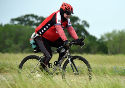 Man riding mountain bike with helmet and sunglasses on grassy trail, demonstrating Bluebonnet Express cycling event.