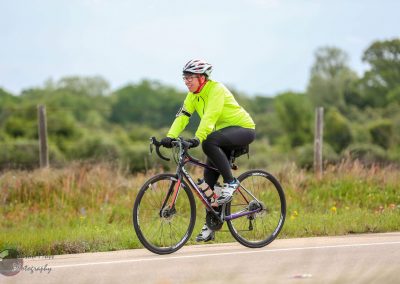 Bright neon cycling jacket and helmet on a female cyclist riding a road bike outdoors in nature.