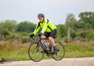 Vibrant cyclist riding a Pinarello road bike on countryside road, promoting Bluebonnet Express cycling event.