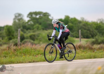 Vibrant female cyclist riding on a scenic rural road with lush greenery and wildflowers, emphasizing outdoor biking adventure.