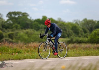 Cyclist riding a road bike outdoors on a scenic trail with greenery and open sky.